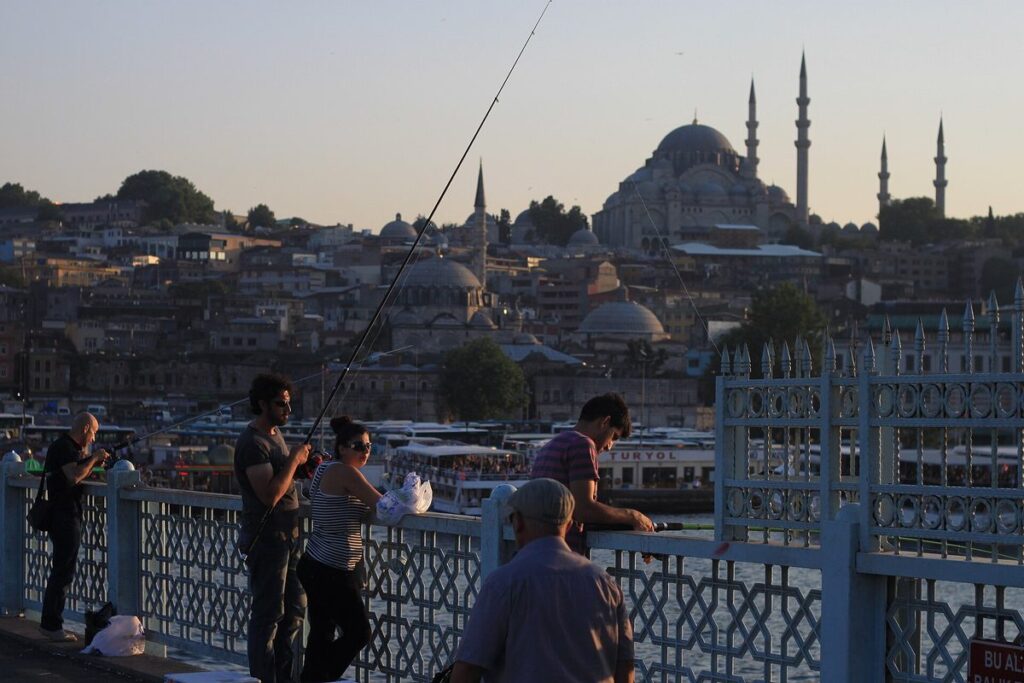 Fishermen on Galata Bridge at dusk with the domes and minarets of the old city of Istanbul behind