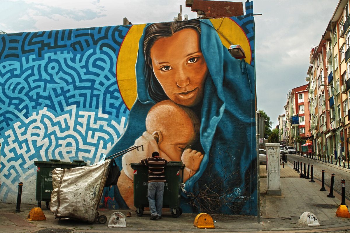 A large mural of a mother and child painted on the side of a building on a Kadikoy street