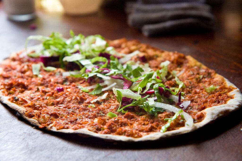 A lahmacun topped with minced lamb, parsley and onion on a wooden board