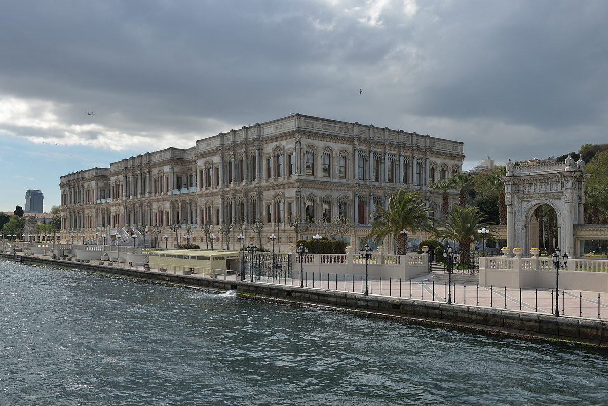 Ciragan Palace stretching along the Bosphorus waterfront under a cloudy sky, with its ornate gate on the right
