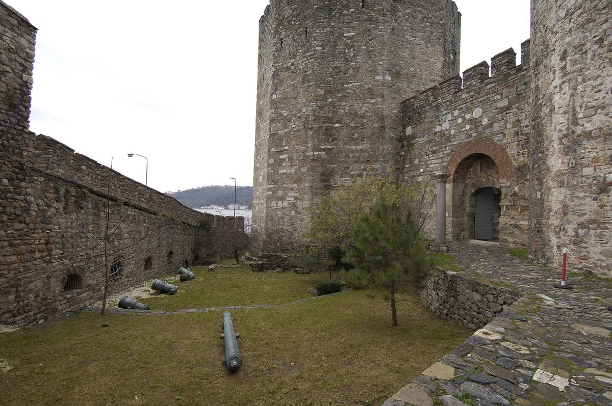 A tower and curtain wall inside Rumeli Hisari fortress, with an old cannon lying on the grass