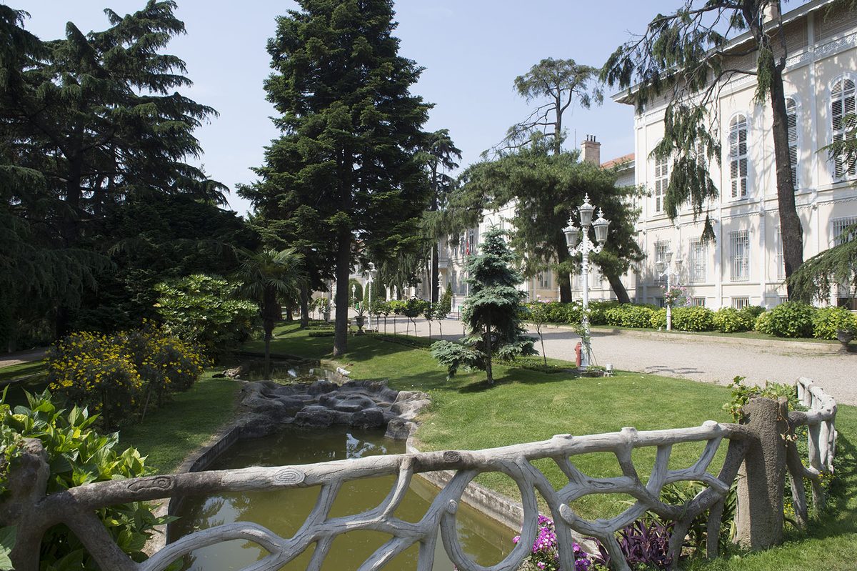 A pond with an ornamental stone balustrade and lawns among tall trees in Yildiz Park